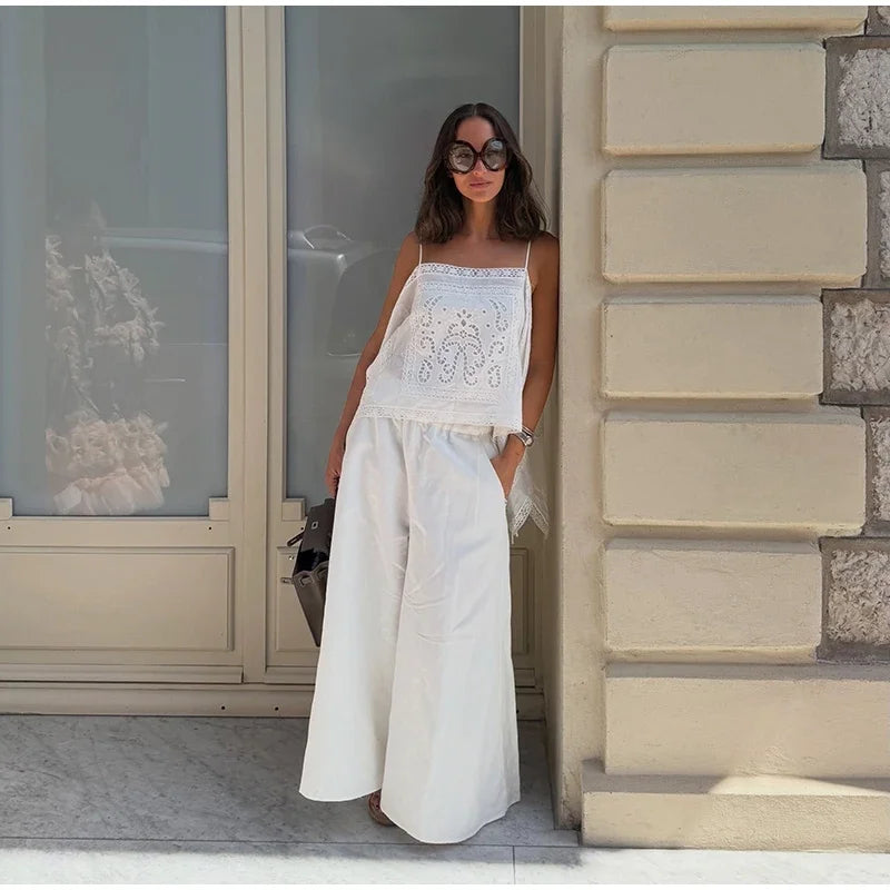 A woman wearing a white sleeveless top embroidered detailing on the bodice and wide-leg pants,